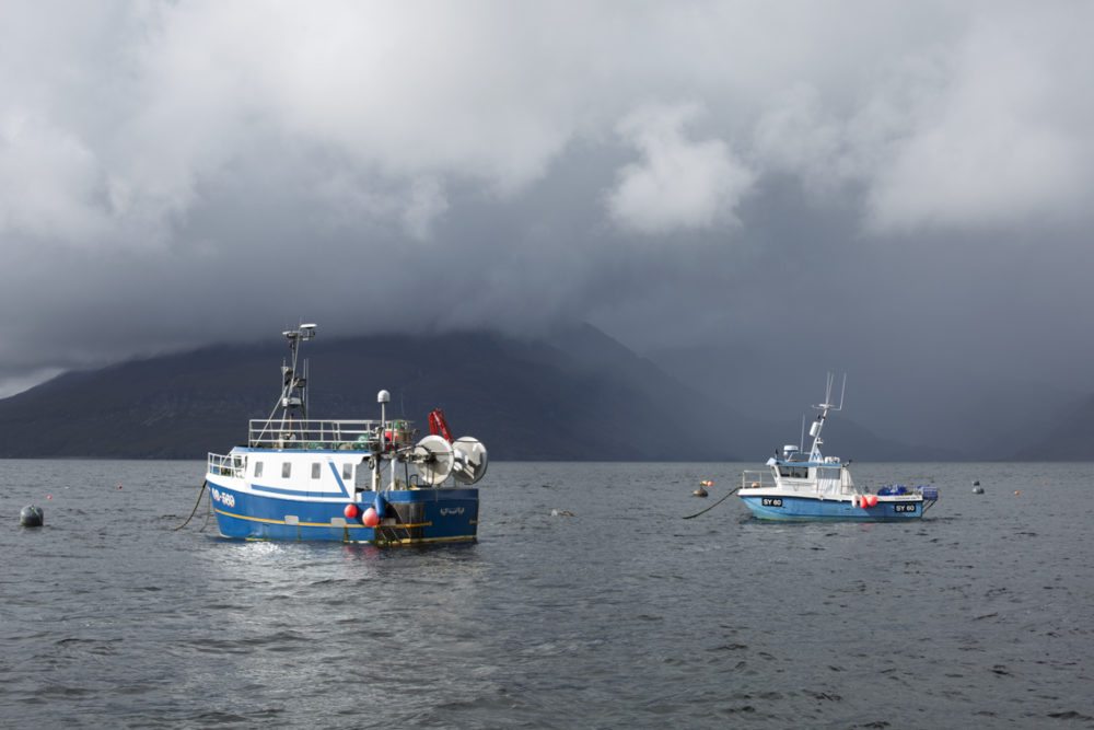 Two fishing boats sitting at anchor in front of the misty Cullin mountains on the Isle of Skye